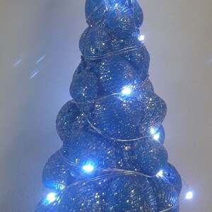 Puede incluir: Un árbol de Navidad azul con purpurina hecho de conchas marinas con luces blancas y una estrella de mar blanca en la parte superior.