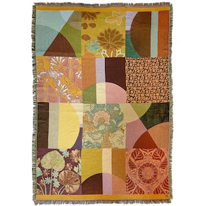 Op de afbeelding: Een geweven deken met een geometrisch patroon in tinten bruin, geel, groen en roze. Het patroon bevat cirkels, vierkanten en rechthoeken.