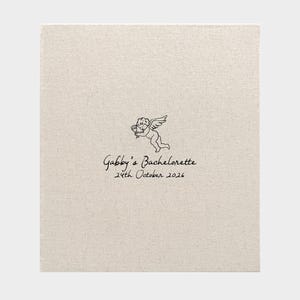 May include: A rectangular, light beige linen-textured cover featuring a black line drawing of a cherub holding a glass. Below the cherub, the text reads "Gabby's Bachelorette" followed by the date "24th October 2026" in a simple black script font.