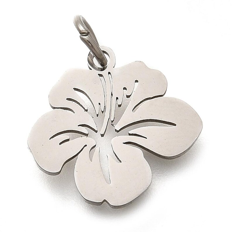 Puede incluir: Un colgante de flor de hibisco plateado con un lazo para sujetarlo a una cadena. El colgante tiene un dise&ntilde;o recortado detallado de los p&eacute;talos y el centro de la flor. El colgante est&aacute; hecho de un material met&aacute;lico brillante.