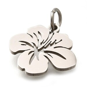 Puede incluir: Un dije de flor de hibisco de color plateado con un dise&ntilde;o calado detallado. El dije tiene un peque&ntilde;o lazo en la parte superior para sujetarlo a un collar o pulsera. Los p&eacute;talos de la flor son lisos y redondeados, con un contorno oscuro.