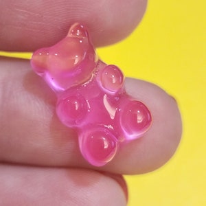 May include: A pink gummy bear candy shaped like a bear with a shiny, translucent finish.