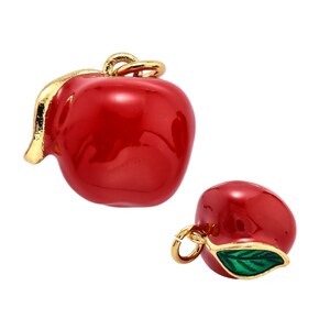 May include: Two gold-toned apple charms with red enamel. One charm has a green enamel leaf.