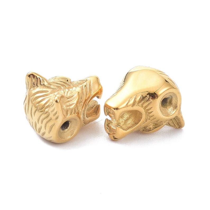 May include: Two gold-toned metal beads shaped like stylized animal heads. Each bead features a polished, reflective surface with detailed engravings representing fur texture and facial features, including a visible hole for threading through the side.