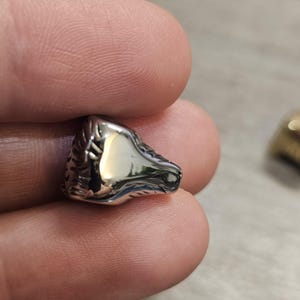 May include: A small, polished silver-toned metal bead shaped like a horse head. The surface is highly reflective with a smooth finish, featuring detailed etched lines along the mane and facial structure, capturing light with a bright metallic sheen.