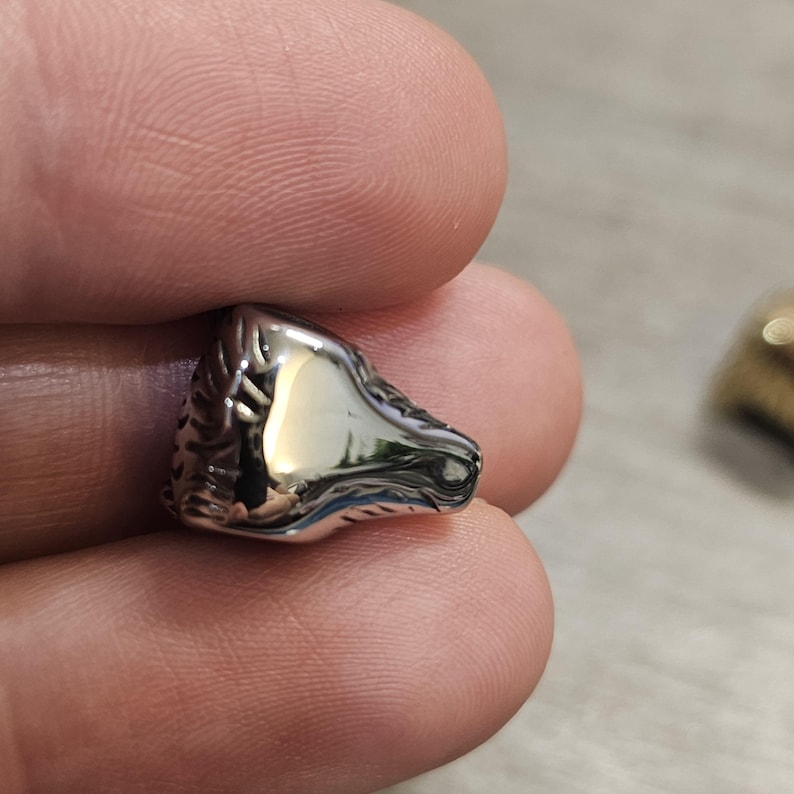 May include: A small, polished silver-toned metal bead shaped like a horse head. The surface is highly reflective with a smooth finish, featuring detailed etched lines along the mane and facial structure, capturing light with a bright metallic sheen.