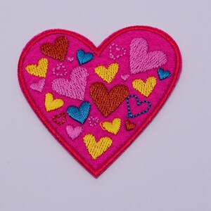 May include: Pink felt heart-shaped patch with embroidered hearts in various colors, including red, yellow, blue, and pink.