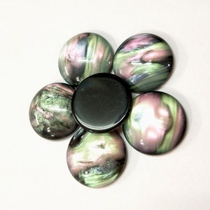 Pode incluir: Seis cabochões redondos e iridescentes em tons de verde, rosa e preto. Os cabochões estão dispostos em forma de flor com um cabochão preto no centro.