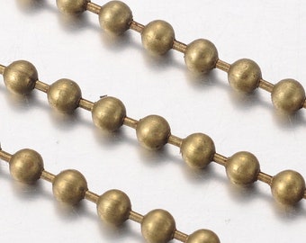 Könnte beinhalten: Nahaufnahme einer goldenen Kugelkette. Die Kette besteht aus kleinen, runden Perlen, die durch dünne Metallglieder verbunden sind. Die Kette liegt auf einer weißen Oberfläche.