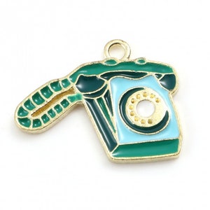 May include: A gold-coloured vintage telephone charm. The charm has a light blue dial and a green handset. The phone is outlined in gold and has a gold loop for attaching to a necklace or bracelet.