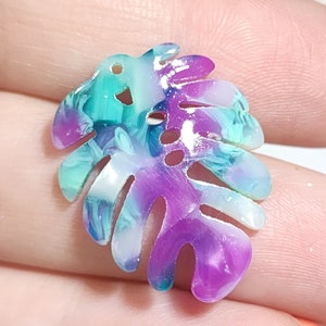 May include: A purple and teal iridescent resin leaf charm with a hole at the top for hanging. The leaf has a marbled pattern and a glossy finish.