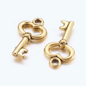 Puede incluir: Dos dijes de llave de color dorado con mirillas en forma de corazón. Los dijes tienen un estilo vintage y son perfectos para agregar un toque de fantasía a las joyas o las manualidades.