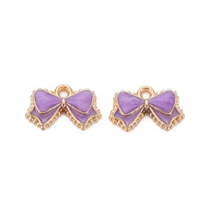 May include: Two gold-toned metal charms shaped like bows with a purple enamel finish. The charms have a loop at the top for attaching to jewelry or other crafts.