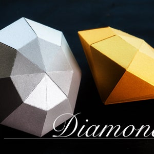 Puede incluir: Dos diamantes de papel, uno plateado y otro dorado, sobre un fondo negro. La palabra "Diamonds" está escrita en cursiva blanca debajo de los diamantes.