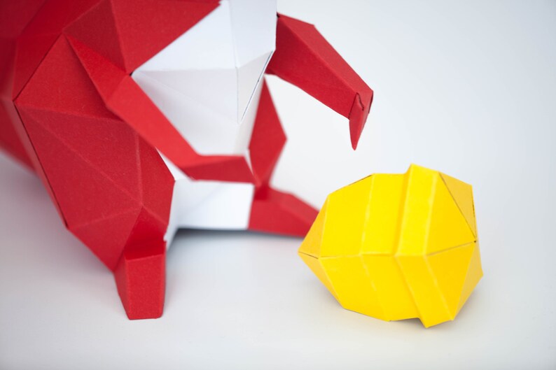 May include: A red and white origami figure with a yellow origami sphere in front of it. The figure appears to be reaching out to the sphere.