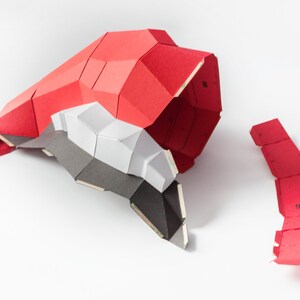 以下が含まれることがあります： 赤、白、黒の紙でできた幾何学的な形のモデル。モデルは部分的に組み立てられており、一部の部品はまだ別々にあります。モデルは厚紙でできており、表面はテクスチャ加工されています。