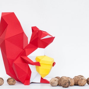 May include: A red origami squirrel holding a yellow origami nut. The squirrel is standing on a white surface with several brown walnuts scattered around it.