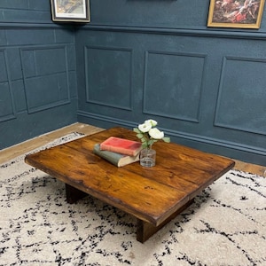 May include: A rustic wooden coffee table with a dark brown stain. The table has a rectangular top and a simple, blocky design. It is sitting on a white rug with a black and white pattern.
