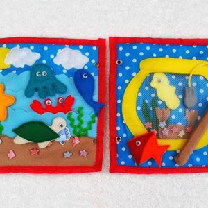 May include: Two felt squares with a blue background and white polka dots. The left square features a felt ocean scene with a yellow sun, blue clouds, a green turtle, a red crab, a blue fish, a green seaweed, a yellow starfish, and an octopus. The right square features a yellow fishbowl with a yellow fish, a gray net, a brown fishing rod, and a red fish.