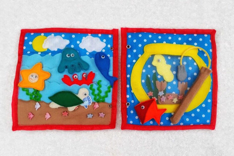 May include: Two felt squares with a blue background and white polka dots. The left square features a felt ocean scene with a yellow sun, blue clouds, a green turtle, a red crab, a blue fish, a green seaweed, a yellow starfish, and an octopus. The right square features a yellow fishbowl with a yellow fish, a gray net, a brown fishing rod, and a red fish.