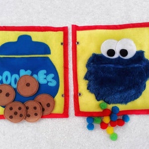 May include: A felt book for children with two pages. The first page has a blue cookie jar with the word "Cookies" on it and brown felt cookies. The second page has a blue felt monster with big eyes and a yellow background. There are colorful felt balls scattered on the page.