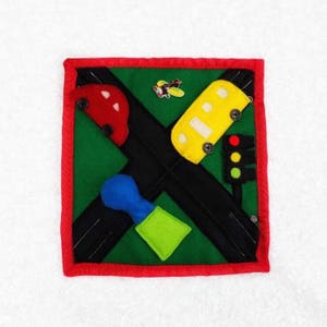 May include: A green felt quiet book with a red car, yellow bus, blue shape, green square, and a red, yellow, and green traffic light. The book has a red border.