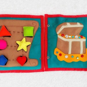 May include: A felt activity book with two pages. The left page has a brown felt shape with a variety of cutouts for different shapes, including a star, a heart, a circle, a square, and a triangle. The right page has a brown felt treasure chest with a yellow felt trim and a variety of colorful jewels.