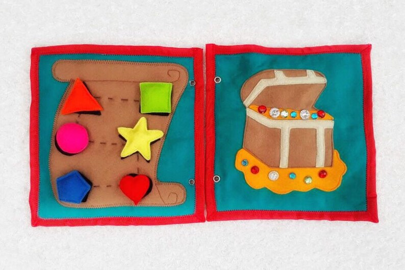 May include: A felt activity book with two pages. The left page has a brown felt shape with a variety of cutouts for different shapes, including a star, a heart, a circle, a square, and a triangle. The right page has a brown felt treasure chest with a yellow felt trim and a variety of colorful jewels.