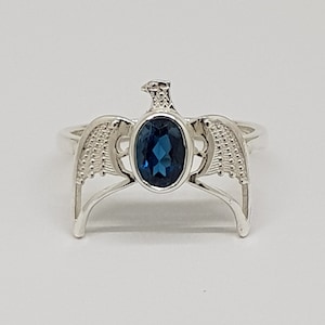May include: A silver ring with a blue gemstone set in a bird wing design.