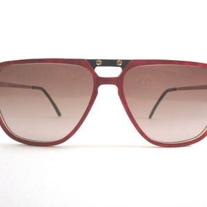 Puede incluir: Gafas de sol aviador rojas con puente negro y detalles dorados. Las lentes son marrones y tienen un degradado.