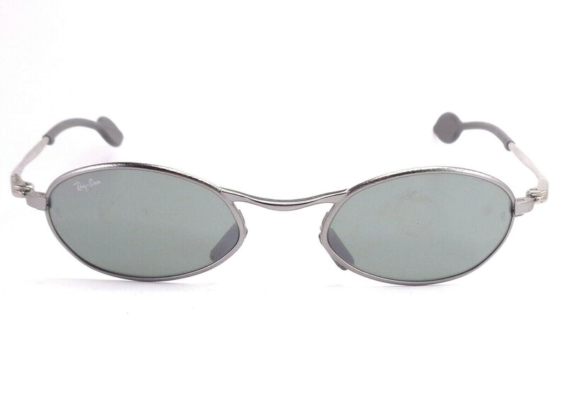 May include: Silver-framed sunglasses with oval lenses and a subtle green tint. The Ray-Ban logo is visible on the left lens. The temples have gray ear pieces. A stylish accessory for eye protection.