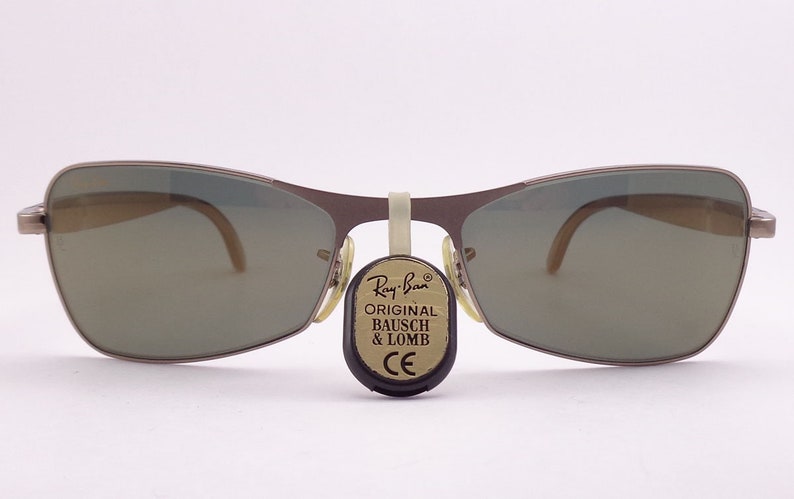 Puede incluir: Un par de gafas de sol Ray-Ban plateadas con lentes verdes. Las gafas tienen una etiqueta que dice "Ray-Ban Original Bausch & Lomb CE".