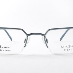 Puede incluir: Gafas de metal gris con montura rectangular. La montura está hecha de beta-titanio y es 100% libre de níquel. El nombre de la marca "MATRIX TITANIO" está impreso en la lente derecha.