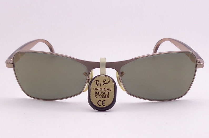 Puede incluir: Un par de gafas de sol Ray-Ban plateadas con lentes marrones. Las gafas tienen una etiqueta adjunta que dice "Original Bausch & Lomb CE".
