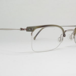 May include: Silver and green half-rim eyeglasses with a clear lens. The brand name "RODENSTOCK" is printed on the right temple.