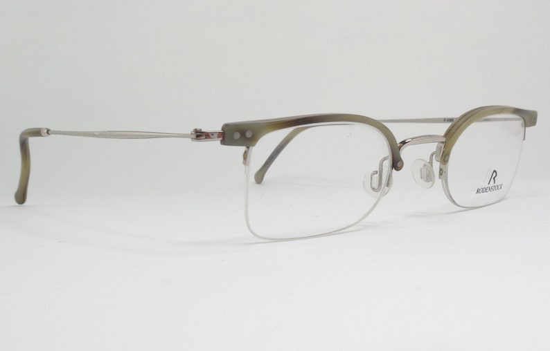 May include: Silver and green half-rim eyeglasses with a clear lens. The brand name "RODENSTOCK" is printed on the right temple.