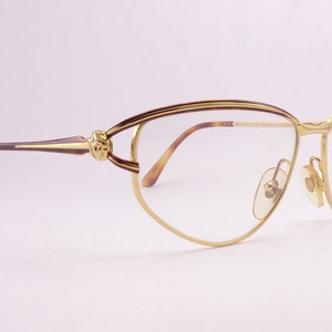 May include: Gold-tone cat-eye glasses with brown tortoise shell arms and a decorative detail on the bridge. The glasses have clear lenses.