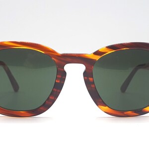 May include: Tortoise shell sunglasses with dark green lenses. The sunglasses have a rounded frame.