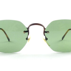 May include: Rimless sunglasses with light green lenses and brown metal frames. The lenses have an octagonal shape. The temples are thin and have a tortoiseshell pattern. The bridge is a dark brown color.