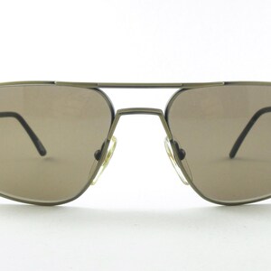 Puede incluir: Un par de gafas de sol aviador marrones con montura de metal. Las gafas de sol tienen lentes marrones oscuros y un acabado dorado.