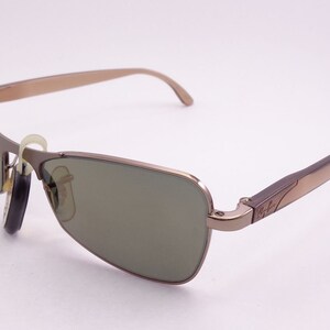 Puede incluir: Un par de gafas de sol aviador de metal marr&oacute;n con lentes verdes. Las gafas tienen el logotipo de Ray-Ban en el lateral.