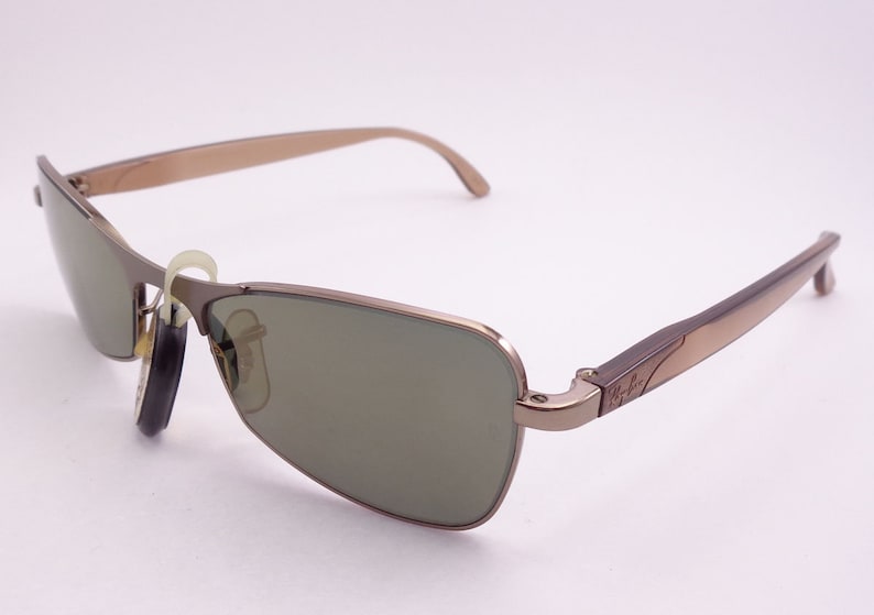 Puede incluir: Un par de gafas de sol aviador de metal marr&oacute;n con lentes verdes. Las gafas tienen el logotipo de Ray-Ban en el lateral.