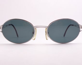 Könnte beinhalten: Silberne ovale Sonnenbrille mit dunkelgrauen Gläsern.