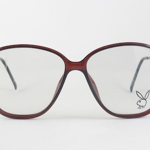 May include: Brown plastic framed glasses with clear lenses. The right lens has a black Playboy bunny logo.