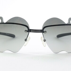 Könnte beinhalten: Schwarze Sonnenbrille mit einem einzigartigen apfelförmigen Rahmen und grauen Verlaufsgläsern.