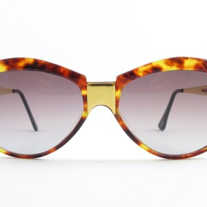 May include: Tortoise shell sunglasses with a gold metal bridge and black arms. The lenses are a gradient brown color.