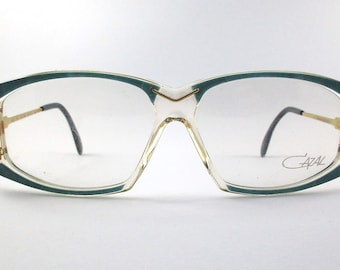 May include: A pair of clear, teal, and gold-rimmed eyeglasses with the Cazal logo on the right temple.