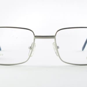 Puede incluir: Gafas rectangulares plateadas con un sistema de oro relleno. El nombre de la marca "Desil Gold Filled" está impreso en la patilla derecha.