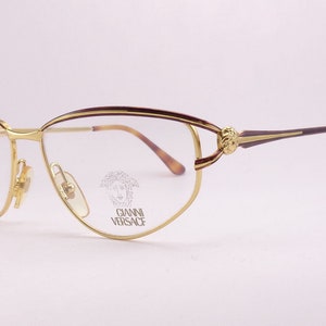 May include: Gold-tone metal eyeglasses with a tortoiseshell frame and a small, engraved logo that says "Gianni Versace" on the right lens.