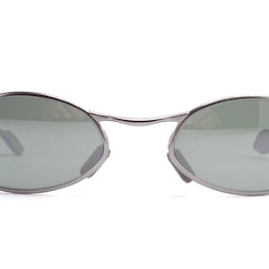 May include: Oval-shaped sunglasses with a silver metal frame and green lenses. The Ray-Ban logo is visible on the left lens. The sunglasses have a classic, minimalist design.